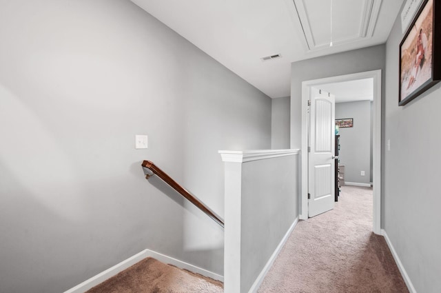 hallway with visible vents, attic access, light carpet, an upstairs landing, and baseboards