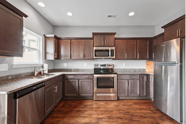 kitchen featuring visible vents, dark wood finished floors, appliances with stainless steel finishes, dark stone countertops, and a sink