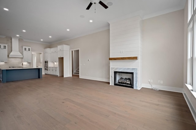 unfurnished living room with light wood-type flooring, a premium fireplace, baseboards, and crown molding