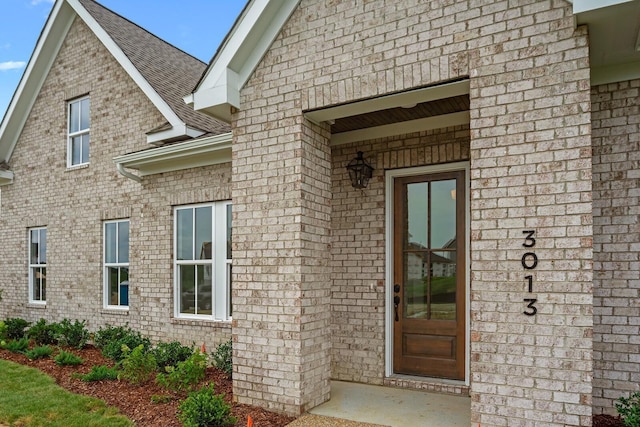 doorway to property featuring brick siding and roof with shingles