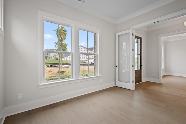 spare room featuring light wood-style floors, crown molding, and baseboards