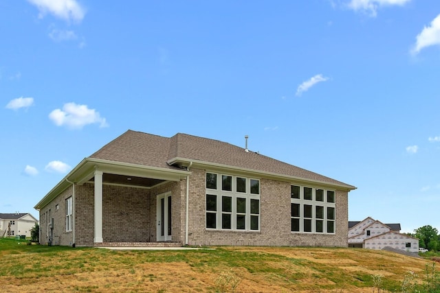 rear view of house featuring a yard, brick siding, and a shingled roof