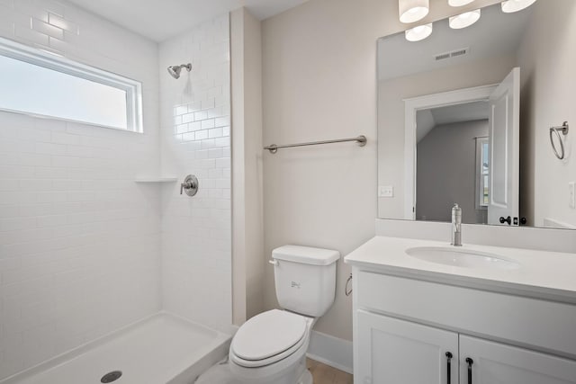 full bath featuring toilet, tiled shower, vanity, and visible vents