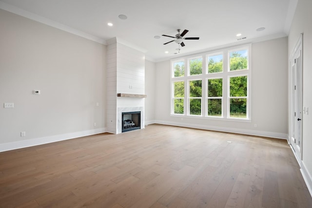 unfurnished living room with baseboards, a high end fireplace, ornamental molding, light wood-type flooring, and recessed lighting