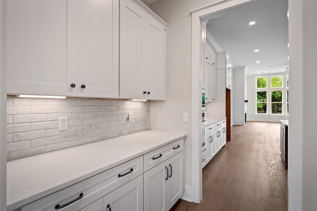 kitchen with wood finished floors, decorative backsplash, light stone countertops, and white cabinets