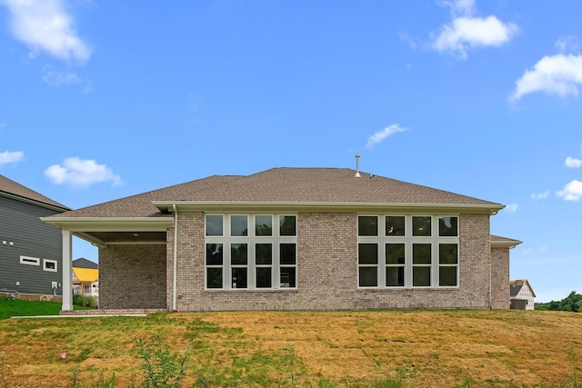 back of house featuring brick siding, a lawn, and a shingled roof