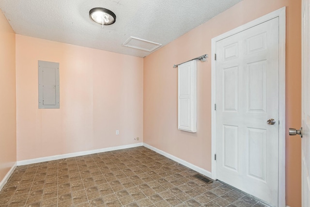 spare room featuring visible vents, attic access, a textured ceiling, electric panel, and baseboards