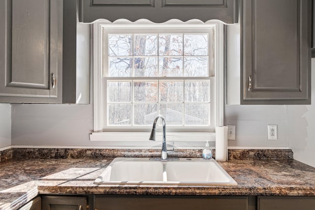 kitchen featuring dark stone countertops, gray cabinets, and a sink