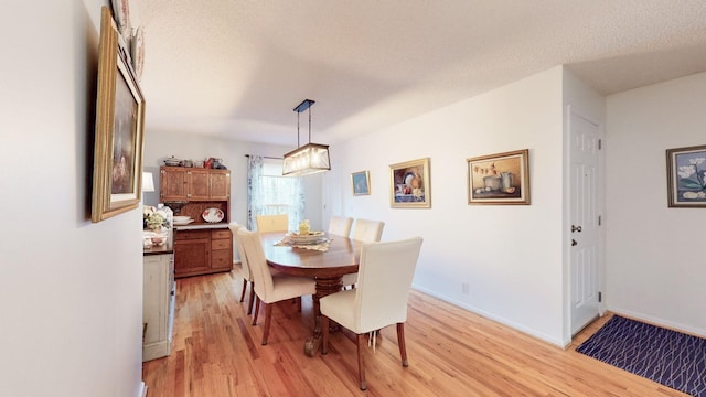 dining space with a textured ceiling, light wood finished floors, and baseboards