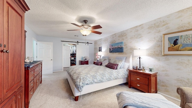 bedroom with wallpapered walls, a barn door, a textured ceiling, and light colored carpet