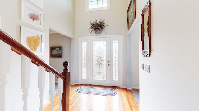 foyer entrance with wood finished floors, a towering ceiling, visible vents, baseboards, and stairway