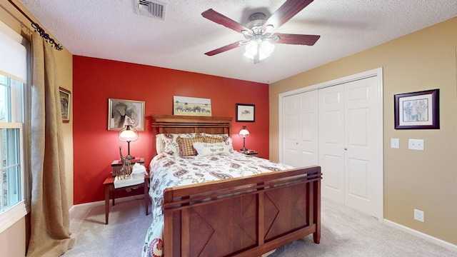 bedroom featuring a textured ceiling, light colored carpet, visible vents, baseboards, and a closet