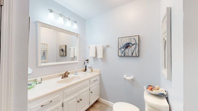 half bath with toilet, baseboards, wood finished floors, and vanity