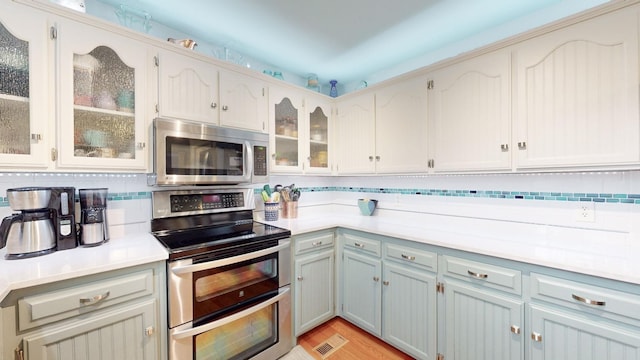 kitchen with stainless steel appliances, tasteful backsplash, light countertops, and glass insert cabinets