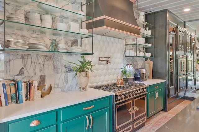 kitchen with tasteful backsplash, range hood, light countertops, double oven range, and open shelves