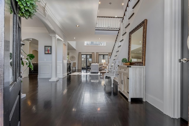 foyer with arched walkways, dark wood-style flooring, a towering ceiling, ornamental molding, and ornate columns