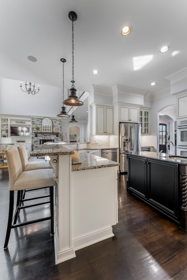 kitchen featuring arched walkways, decorative light fixtures, appliances with stainless steel finishes, glass insert cabinets, and a peninsula