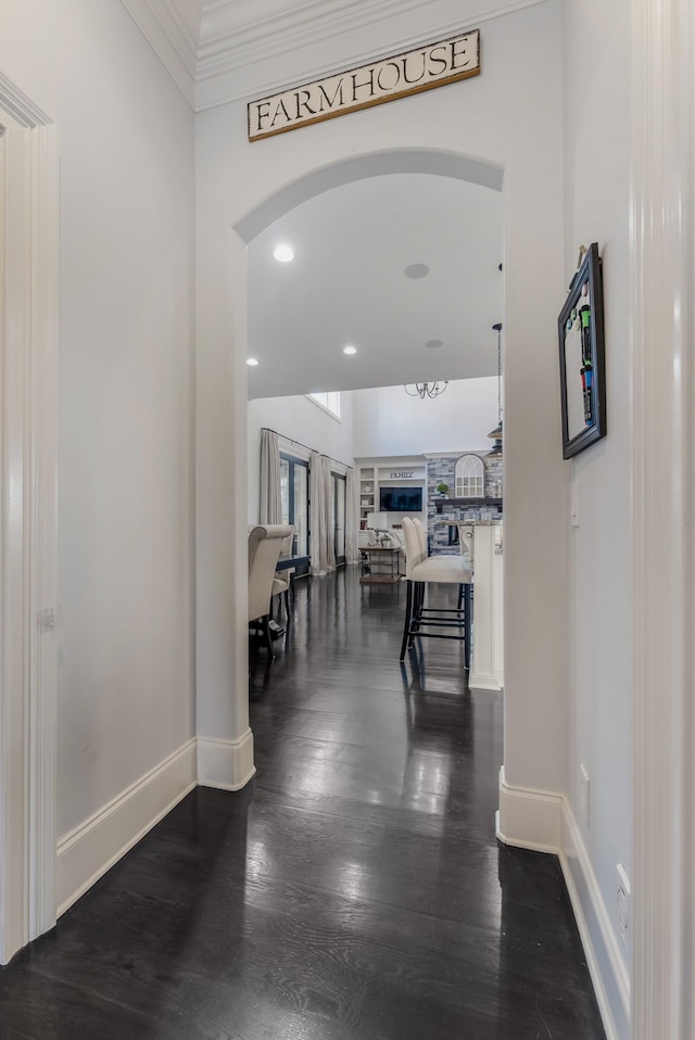 hall featuring ornamental molding, arched walkways, baseboards, and wood finished floors