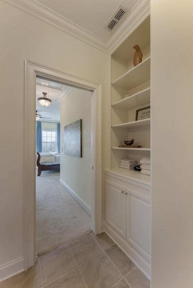 hall with baseboards, visible vents, light colored carpet, ornamental molding, and light tile patterned flooring