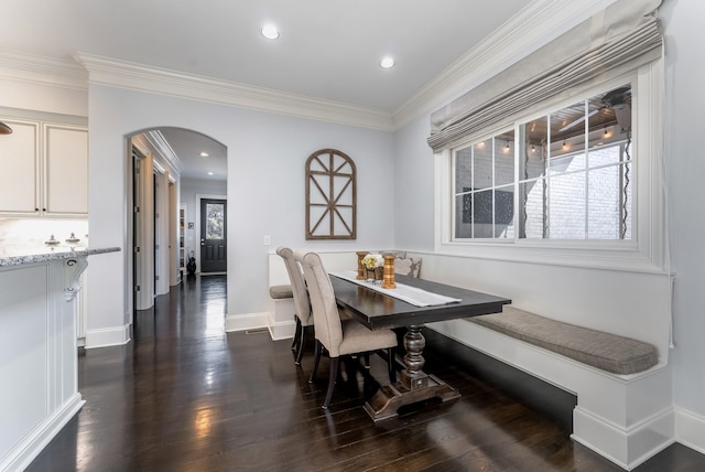 dining area featuring arched walkways, baseboards, ornamental molding, breakfast area, and dark wood finished floors