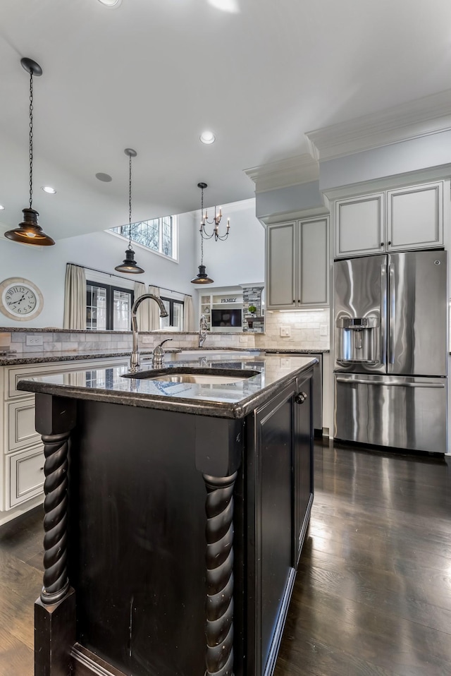 kitchen with pendant lighting, decorative backsplash, an island with sink, dark stone countertops, and stainless steel fridge