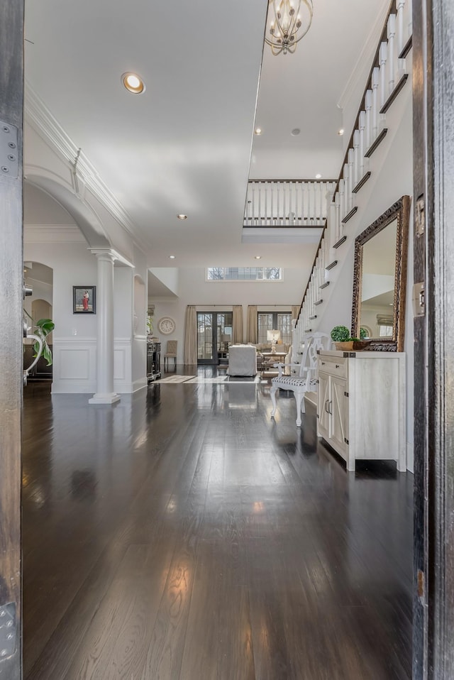 foyer entrance with arched walkways, ornamental molding, stairway, dark wood finished floors, and ornate columns