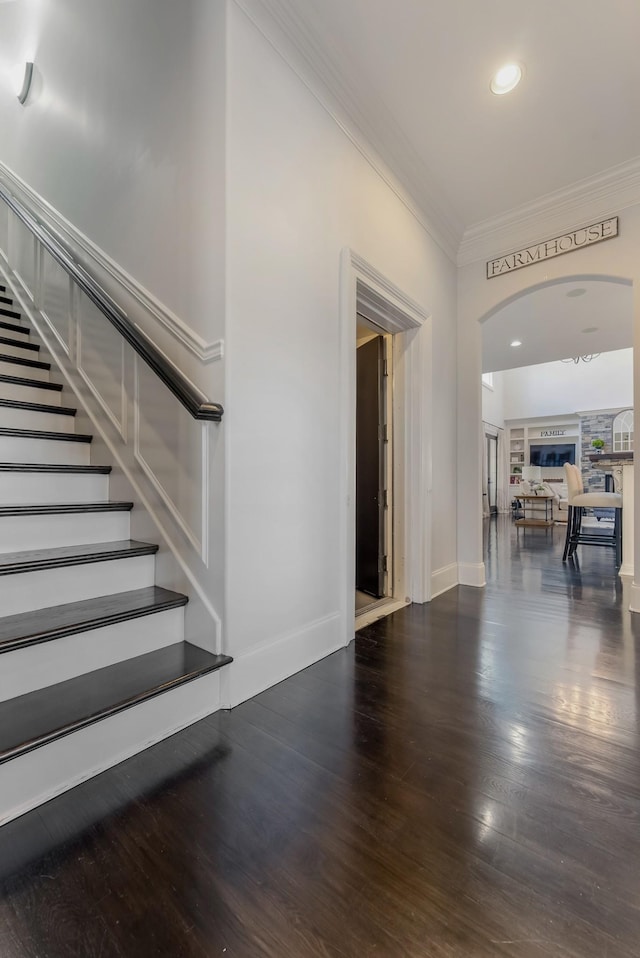 interior space featuring baseboards, arched walkways, wood finished floors, stairs, and crown molding