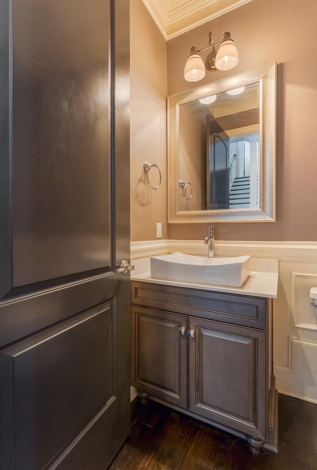 bathroom featuring crown molding, a decorative wall, wainscoting, vanity, and wood finished floors