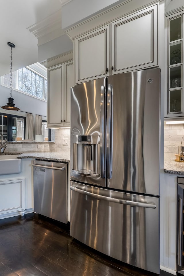 kitchen with light stone counters, appliances with stainless steel finishes, a sink, and glass insert cabinets