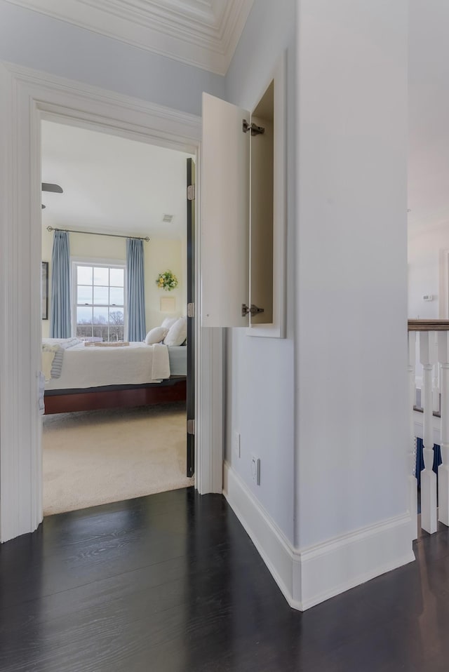 hall featuring dark wood-type flooring, visible vents, ornamental molding, and baseboards