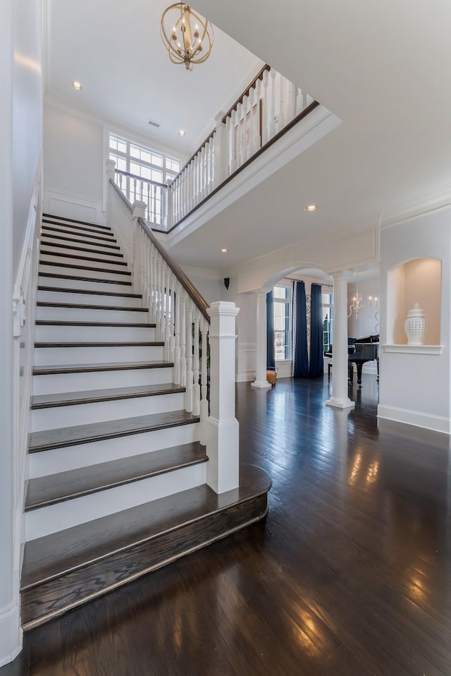 staircase with a wealth of natural light, arched walkways, ornate columns, and wood finished floors