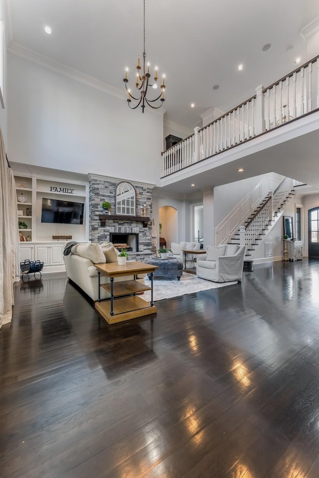 living area featuring a notable chandelier, dark wood-style flooring, a towering ceiling, stairs, and crown molding