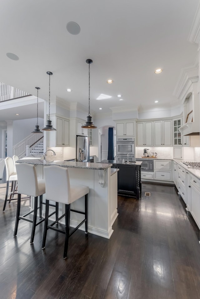 kitchen featuring a center island with sink, a kitchen breakfast bar, decorative light fixtures, stainless steel appliances, and white cabinetry