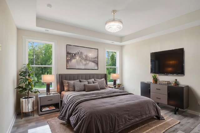 bedroom with a tray ceiling, baseboards, and light wood finished floors