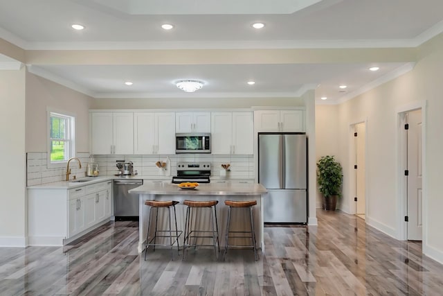 kitchen with light countertops, appliances with stainless steel finishes, white cabinets, a kitchen island, and a sink