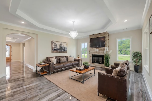 living area featuring arched walkways, a raised ceiling, a stone fireplace, and wood finished floors