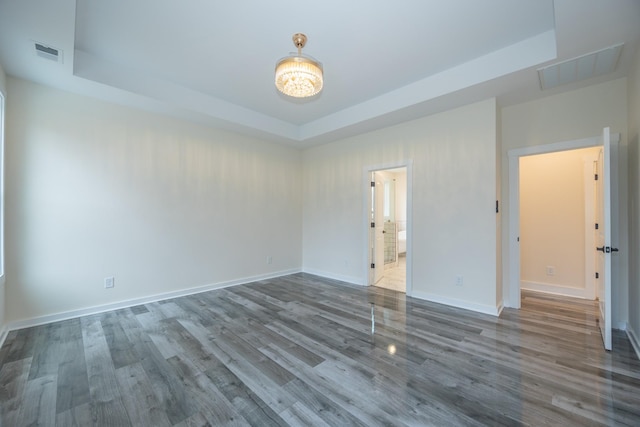 unfurnished room featuring a tray ceiling, visible vents, baseboards, and wood finished floors