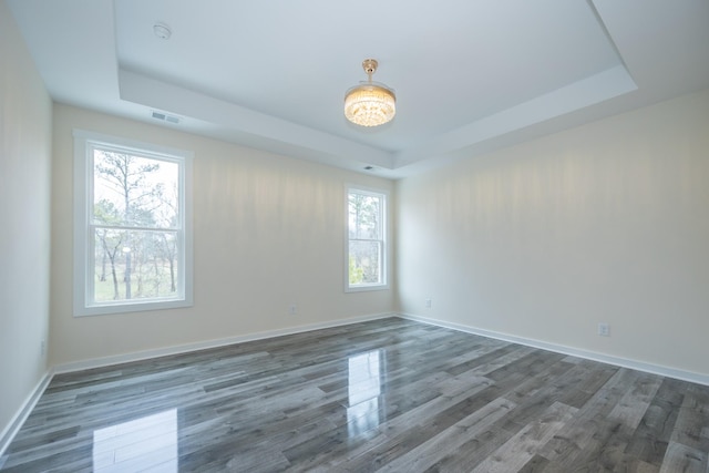 unfurnished room featuring a raised ceiling, visible vents, dark wood finished floors, and baseboards