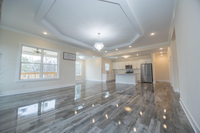 unfurnished living room with recessed lighting, baseboards, a tray ceiling, an inviting chandelier, and crown molding