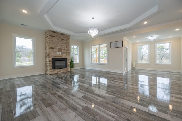 unfurnished living room featuring a tray ceiling, a notable chandelier, a fireplace, visible vents, and baseboards