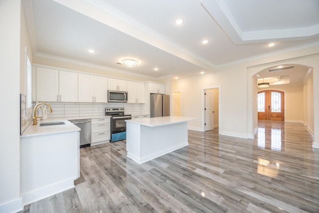 kitchen featuring arched walkways, stainless steel appliances, a sink, white cabinets, and light countertops