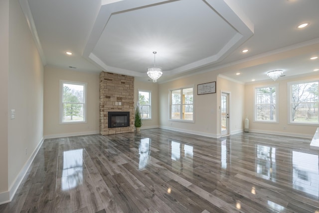 unfurnished living room featuring a chandelier, a tray ceiling, a fireplace, and ornamental molding