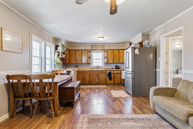 kitchen with crown molding, high end fridge, light countertops, light wood-style flooring, and brown cabinetry