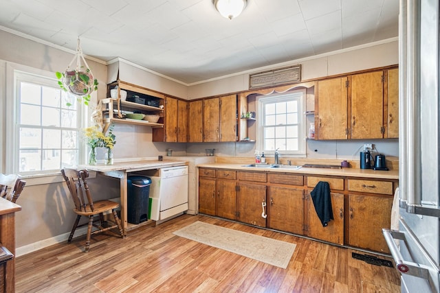 kitchen with a sink, light countertops, ornamental molding, light wood finished floors, and brown cabinetry