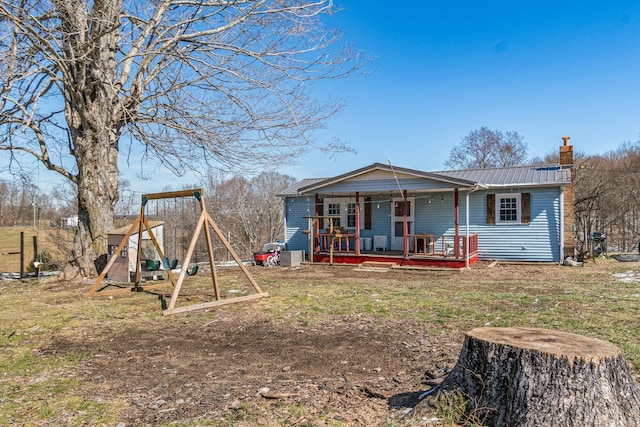 view of front of property featuring covered porch, a chimney, metal roof, and a playground