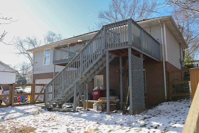 snow covered rear of property featuring stairs, a deck, and brick siding