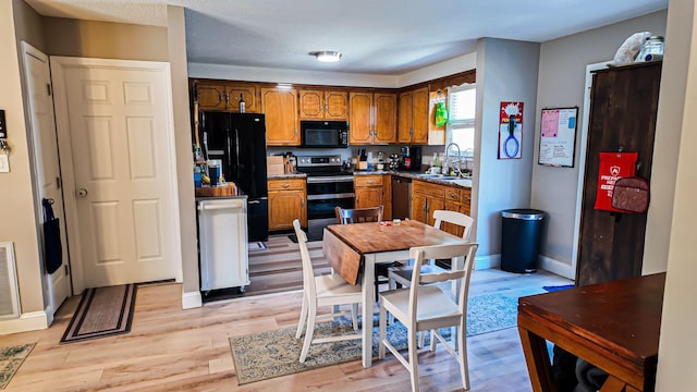 kitchen with brown cabinets, a sink, black appliances, light wood-type flooring, and baseboards