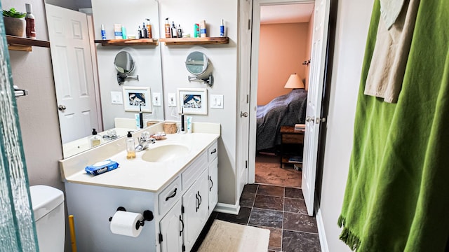 ensuite bathroom featuring toilet, stone tile floors, vanity, baseboards, and ensuite bath