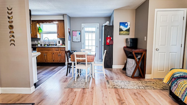 kitchen with baseboards, dark countertops, brown cabinets, light wood-type flooring, and a sink