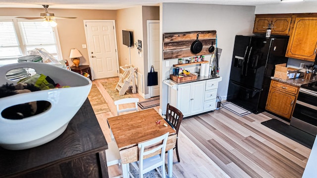 kitchen with brown cabinets, black fridge with ice dispenser, light wood-style floors, a ceiling fan, and stainless steel range with electric stovetop